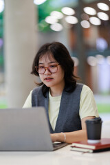 Fototapeta premium Young Asian woman wearing glasses and a vest. Focused on her laptop screen