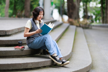 Obraz premium Young female student sitting on outdoor steps, deeply engrossed in reading a book, representing concepts of learning, study, and concentration on education