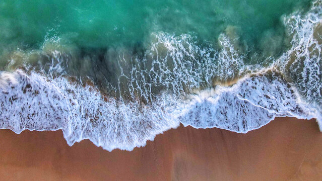 Aerial view of the turquoise waves of the Pacific Ocean crashing onto the sandy shore of Parque Nacional Cabo Pulmo in Cabo Pulmo, Baja California Sur, Mexico.