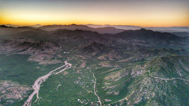 Aerial view of Parque Nacional Cabo Pulmo featuring rugged mountain terrain, winding dirt roads, and lush desert vegetation under a soft golden hour sky in Cabo Pulmo, Baja California Sur, Mexico.