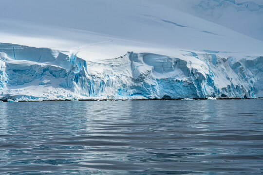 Aerial view of the massive Antarctic glacier with deep blue ice formations and snow-covered slopes meeting the dark ocean waters in Antarctica.