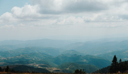 Layered mountain ridges fade into haze beneath summer clouds in Kopaonik, Serbia. The panorama suits travel, tourism, nature and outdoor recreation themes © Ekaterina