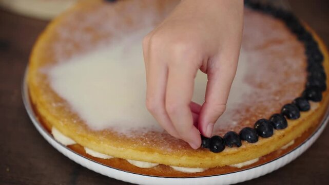 Child's hand decorating cake with blueberry halves close up