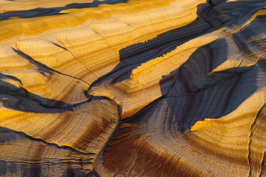 Aerial view of Tiramisu Hills featuring dramatic layered rock formations with golden and dark brown strata under soft sunlight in Kyzylkum, Mangystau Region, Kazakhstan.