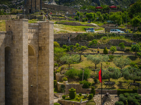 Aerial view of the historic Kruje Castle with its ancient stone walls, terraced gardens, olive trees, and the red flag of Albania fluttering in the breeze in Kruje, Durres County, Albania.