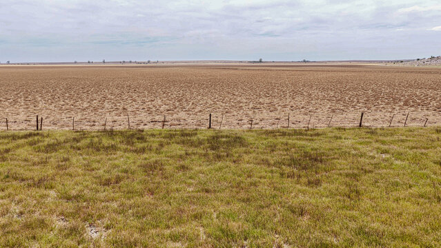 Aerial view of the arid Karoo landscape, featuring dry textured earth, a wire fence line, and sparse grass under a cloudy sky in Beaufort West, Western Cape, South Africa.