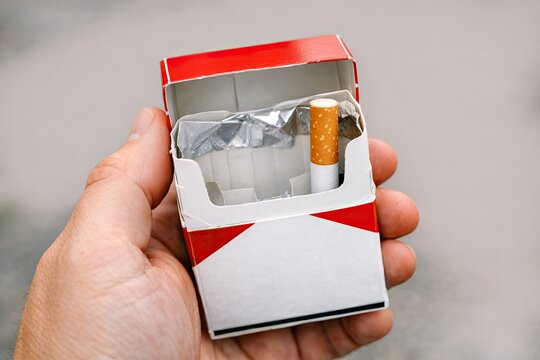 A close-up image of a hand holding a pack of cigarettes inside a box