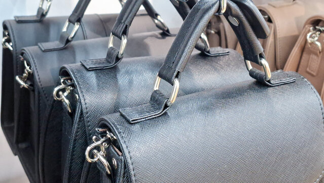 Close up of black saffiano leather handbags with top handles and silver metal hardware displayed in a row at a retail store