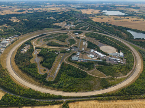 Aerial view of Millbrook Proving Ground, a vehicle testing facility with a large circular track, various test circuits, and surrounding woodland in Bedford, England, United Kingdom.