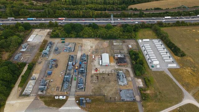 Aerial view of National Grid Sundon Substation featuring electrical transformers, power infrastructure, and battery storage units adjacent to a busy motorway in Chalton, England, United Kingdom.
