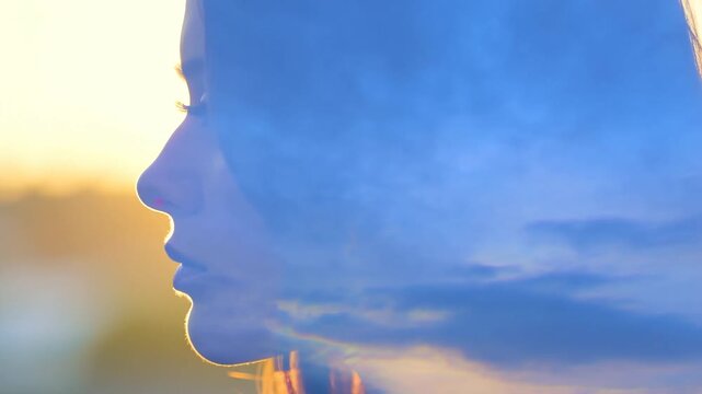 Woman in side profile facing warm sunlight outdoors with blue flare and still posture