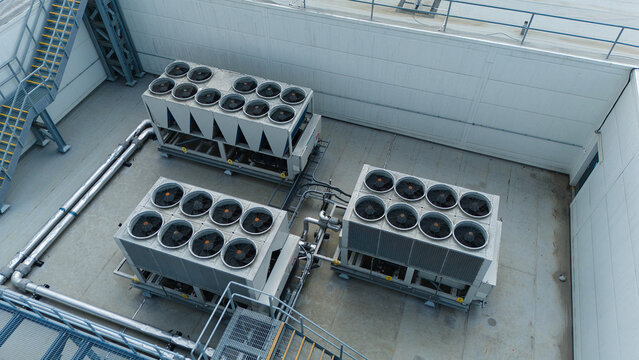 Aerial view of ventilation cooling units, heat exchangers and HVAC fans installed on a flat industrial rooftop in Luton, England, United Kingdom.