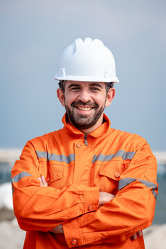 Refinery Engineer Smiling with Arms Crossed in Orange Protective Coveralls and a White Hard Hat while Standing Outdoors at a Petrochemical Industrial Facility during a Work Shift