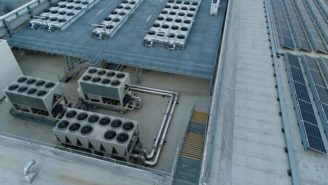 Aerial view of ventilation cooling units, heat exchangers, and HVAC fans installed on a flat industrial rooftop alongside rows of solar panels in Luton, England, United Kingdom.