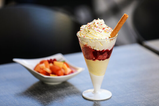 Layered fruit dessert with whipped cream, sprinkles and wafer