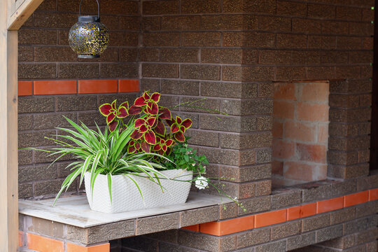 Rustic outdoor brick fireplace with textured brown masonry, orange brick accents, and decorative potted plants on a covered patio
