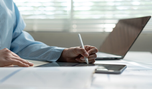 Businesswoman using a stylus on a tablet with laptop in a modern office, analyzing digital data for financial planning, productivity, business strategy and informed decision making.