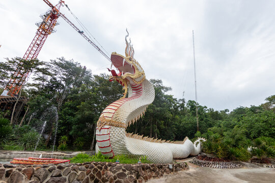 Large white naga serpent statue with open mouth standing near trees and fountain at a temple construction site.