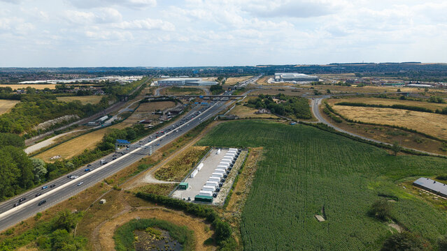 Aerial view of the BESS energy storage facility with rows of white containers situated next to the M1 motorway, surrounded by green fields and rural landscape in Sundon, England, United Kingdom.