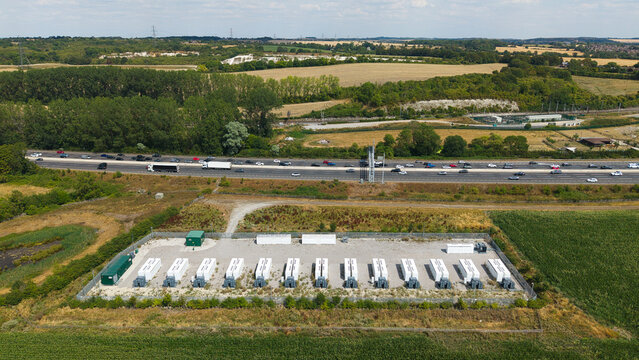Aerial view of the BESS Battery energy park next to the M1 motorway, featuring rows of white storage units and electrical infrastructure surrounded by rural fields in Sundon, England, United Kingdom.