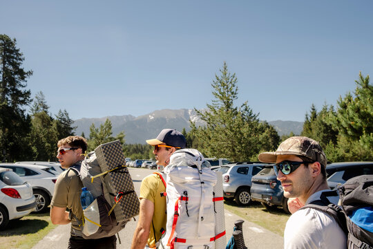 Friends with backpacks in mountain parking lot before hike