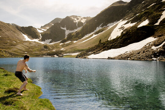 UGC Man skipping stones on alpine lake during Pyrenees hike