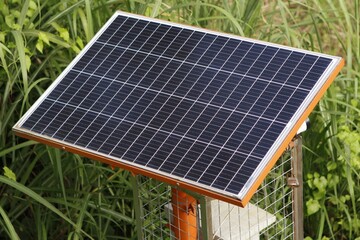 Solar panel mounted on a metal stand surrounded by green grass and plants outdoors © IFAN