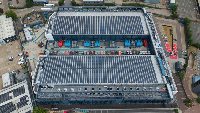 Aerial view of a data center facility featuring solar panel arrays, industrial HVAC cooling units, and surrounding parking areas in Hemel Hempstead, England, United Kingdom.