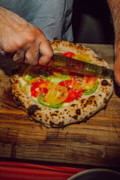 Chef hands cutting a fresh artisanal vegan pizza with a knife