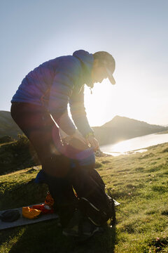 Man packing backpack at sunrise beside alpine lake in Pyrenees