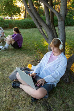 Student using laptop with headphones outdoors while studying
