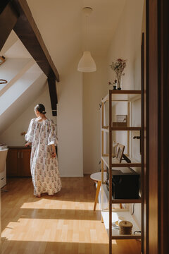 Rear view of  woman in a floral dress standing in a sunlit attic room
