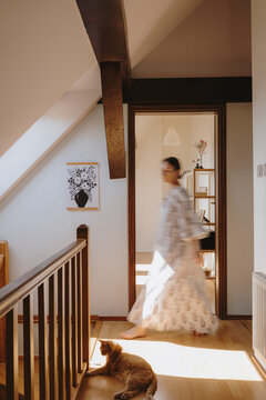 Motion blur of a woman walking past her cat in a sunlit attic hallway