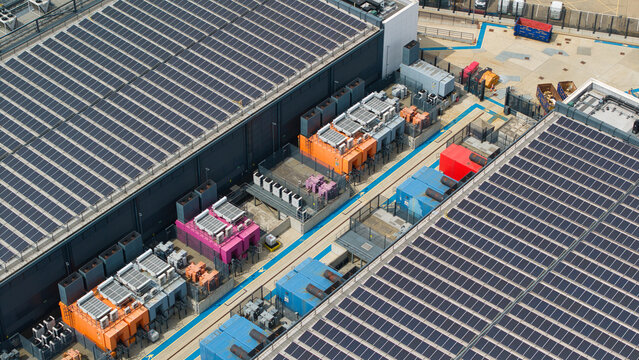 Aerial view of a data center roof featuring rows of solar panels and colorful industrial HVAC cooling units in Hemel Hempstead, England, United Kingdom.