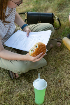 Student reading study notes while eating burger outdoors