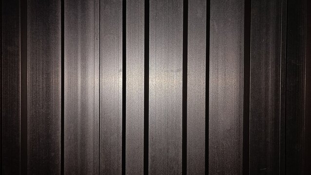 Dark corrugated metal wall panel background with vertical lines and central lighting effect, dramatic metal texture photo