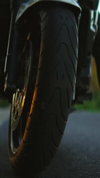 Close-up cinematic view of a powerful motorcycle front wheel with detailed brake disc and tire texture rolling along an empty asphalt road at sunset light