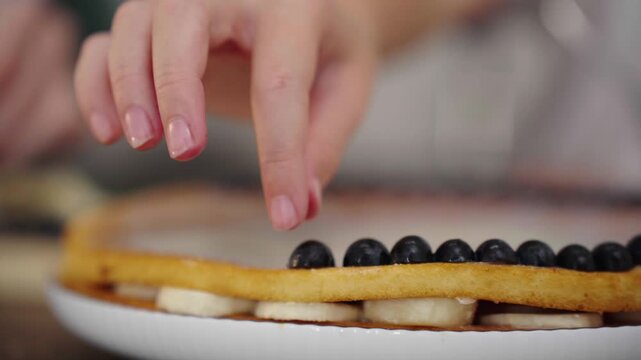 Child's hand decorating cake with blueberry halves close up