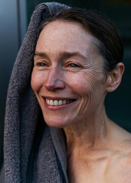Close-up portrait of a middle-aged woman with a towel wrapped around her head. she is smiling widely and appears to be happy and relaxed.