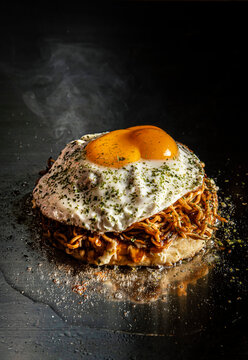 Okonomiyaki pancake with noodles and fried egg on a teppanyaki grill