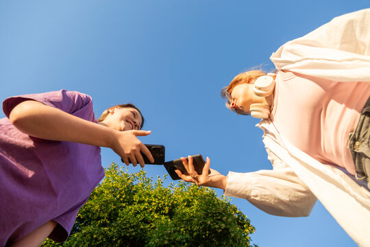 Two young women sharing smartphone outdoors on sunny day