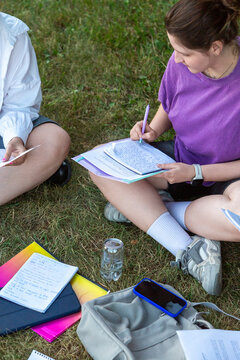 Two students studying together on grass with notes and papers