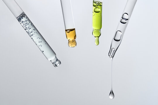 Glass pipettes with different liquids on gray backdrop with copy space