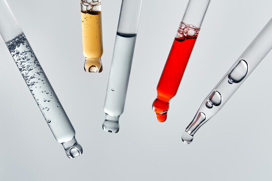 Glass pipettes with different liquids on gray backdrop with copy space