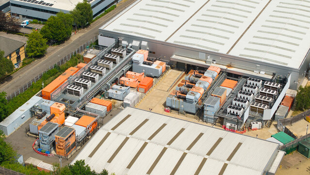 Aerial view of a modern data center facility featuring rows of industrial external cooling units and ventilation systems on the rooftop in Hemel Hempstead, England, United Kingdom.