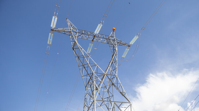 Torre met&aacute;lica de alta tensi&oacute;n con cables y aisladores bajo un cielo azul con nubes blancas