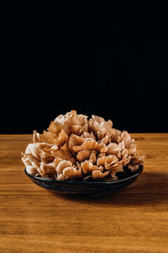 Fresh maitake mushrooms in a dark bowl on a wooden table