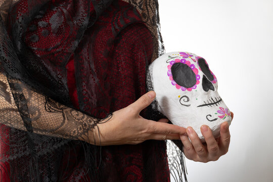 Studio portrait of a woman gently cradling a hand-painted sugar skull, honoring Dia de los Muertos with vibrant color, floral symbolism, and generous copy space for branding and editorial design.