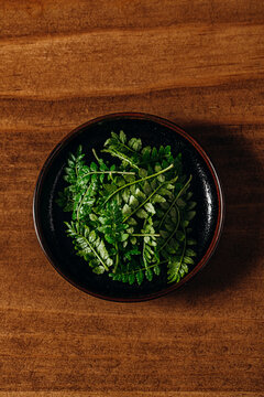 Overhead view of fresh green sansho leaves in a small dark bowl