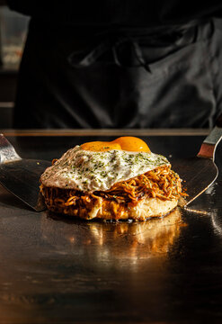 Chef presenting okonomiyaki with fried egg on a teppanyaki grill